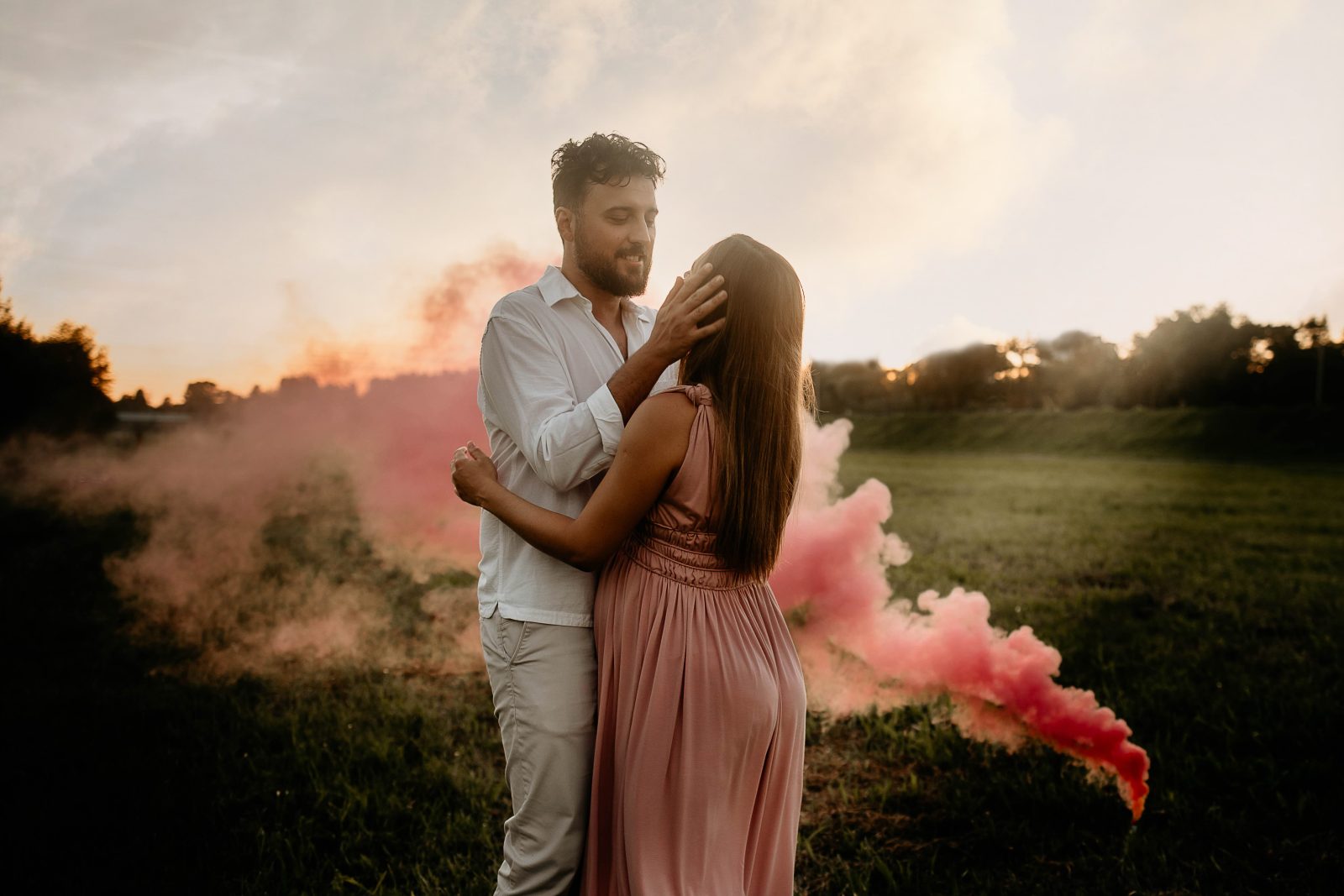 Par u zagrljaju u ružičastom dimu tijekom trudničkog fotografiranja