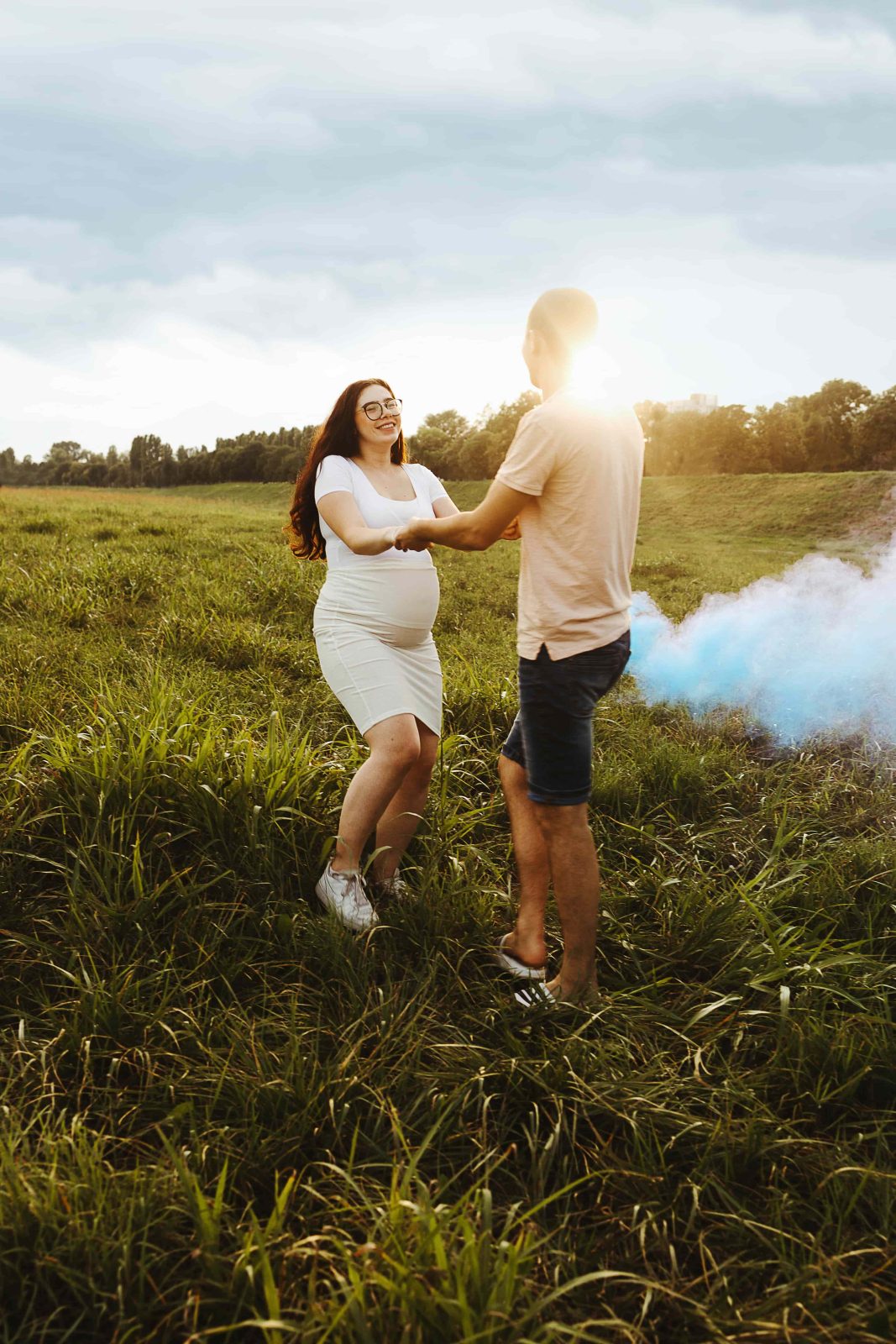 Trudnica i partner stoje na livadi dok ih okružuje plavi dim